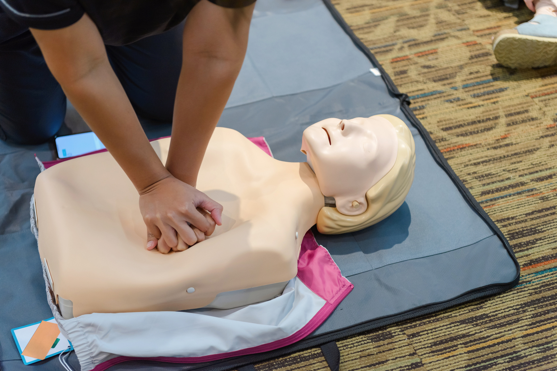 CPR First Aid Training with CPR dummy in the class. Demonstrating chest compressions concept.